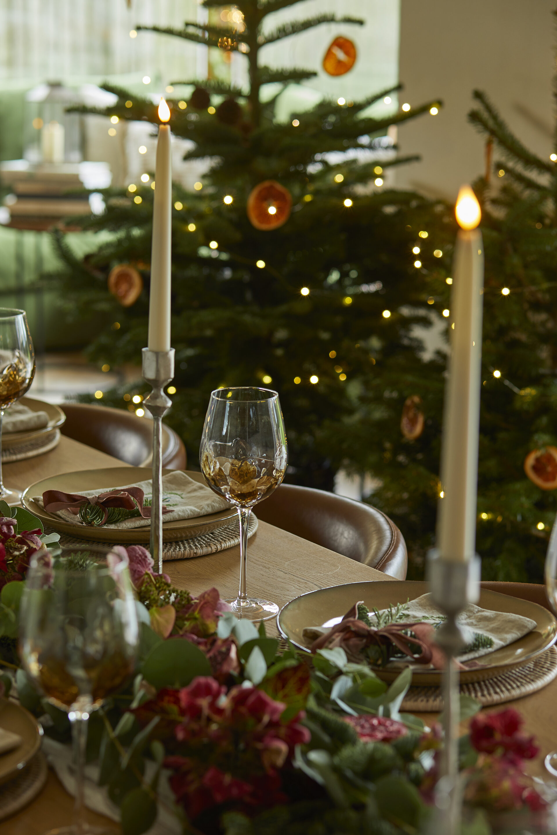 Christmas tree with dried orange ornaments beside candlelit table