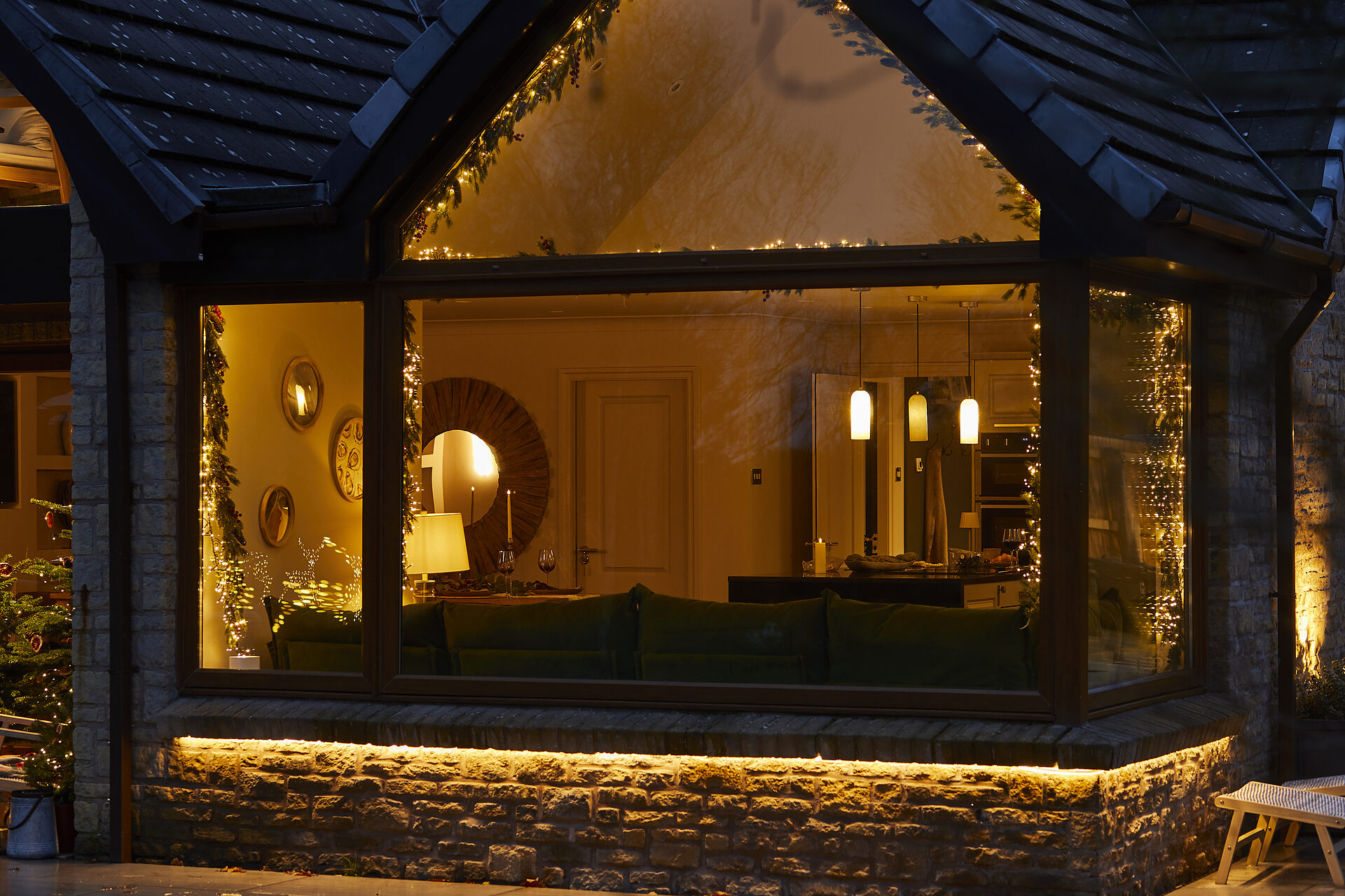 Warren House living room glowing through floor-to-ceiling windows draped with Christmas garlands
