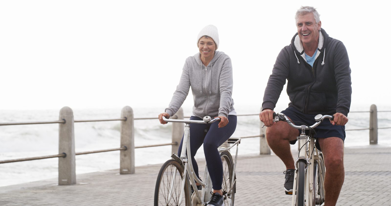 An older couple cycling side by side along a seaside promenade