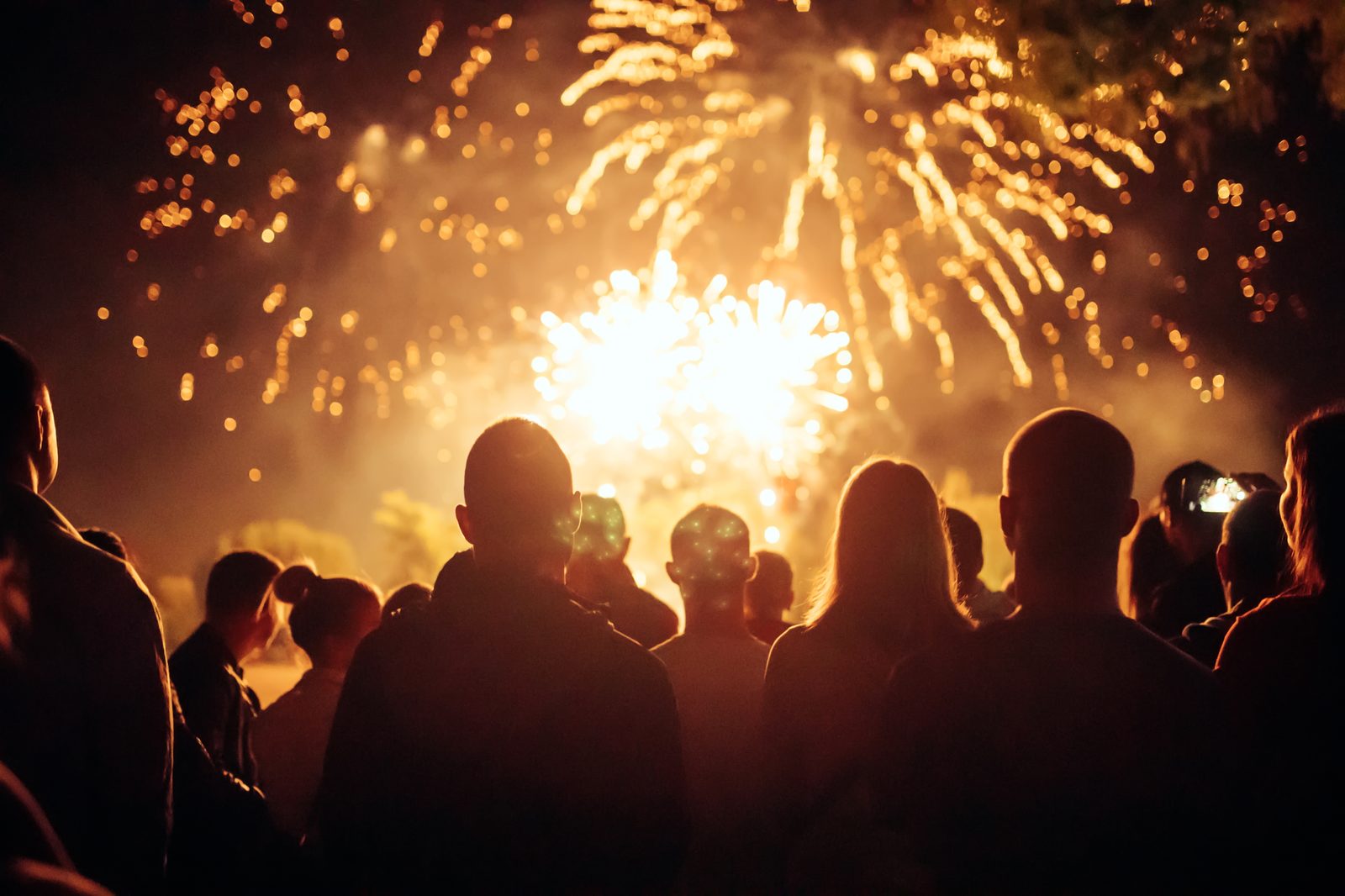 A crowd silhouetted against golden fireworks filling the night sky