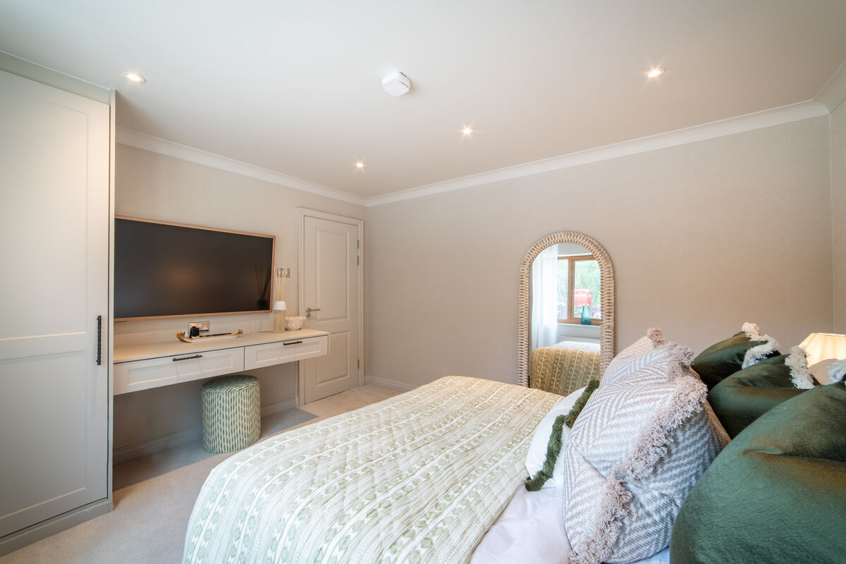 Bedroom six with neutral tones, green cushions, wicker mirror and garden views