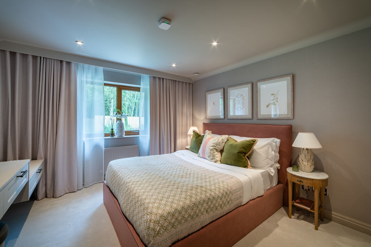 Rose bedroom with pink headboard, grey walls, botanical prints and green cushions